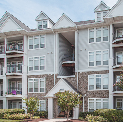 Exterior view of Jefferson Arbors at Broadlands with balconies, trees and lush landscaping - luxury apartments in ashburn va